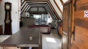 Una zona de menjador amb taula de fusta, un rellotge i vista a la cuina.