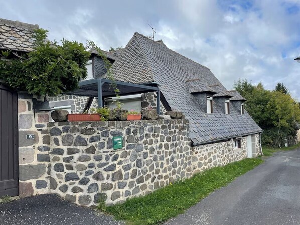 A stone building with a sloped roof, a small porch, and a stone wall with a mailbox.
