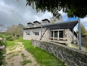 A stone house with a covered patio, a stone wall, and a grassy garden.