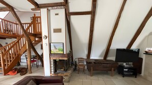 Un saló d'estil loft amb bigues de fusta a la vista, una llar de foc, un televisor i una zona de menjador.