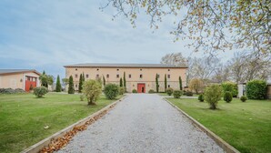 Un edificio con un vialetto ghiaioso che conduce a una porta rossa, immerso nel verde di prati e siepi curate.