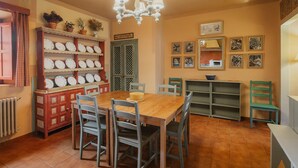 Zona pranzo con tavolo e sedie in legno, un lampadario, una mensola a parete con piatti e una porta con decoro a reticolo.