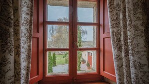 Una habitación con un ventanal grande, cortinas y vistas a un jardín y un edificio.