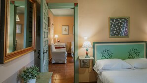 Habitación de hotel con cama, mesita de noche, lámpara, silla, espejo y un cuadro en la pared.