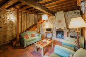 A rustic interior with a stone wall, wooden beams, a fireplace, and a green sofa.