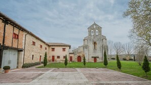 Une cour avec un bâtiment en pierre, une église dotée d’un clocher et un chemin pavé.