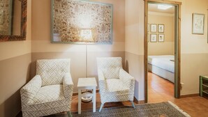 Une pièce avec deux fauteuils à motifs, une petite table, une lampe fixée au mur et un lit à l’arrière-plan.