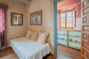 Une chambre avec un lit, un miroir, un tableau représentant des fleurs et une vue sur la cuisine.