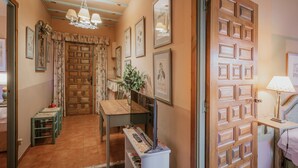 Un couloir avec une porte en bois, des tableaux encadrés, une table avec une lampe et un téléviseur.