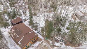 A two-story house with a brown roof and a small porch, surrounded by snow-covered ground and trees. - The Nordico Point Cabin (Ely)