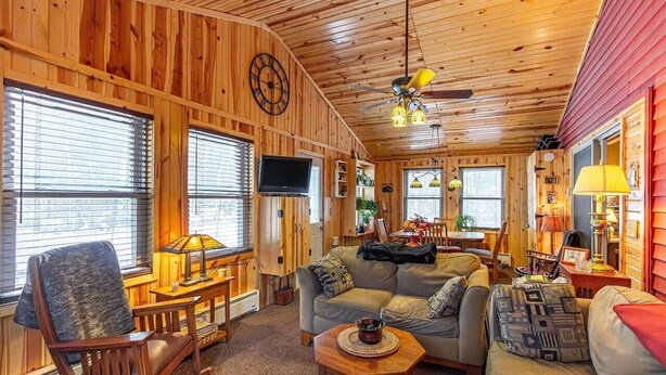 A cozy cabin interior with wooden walls, a ceiling fan, a television, and a dining area. - The Nordico Point Cabin (Ely)