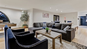 Ein modernes Wohnzimmer mit einer Couch, zwei Sesseln, einem Couchtisch und einem Essbereich mit Tisch und Stühlen.