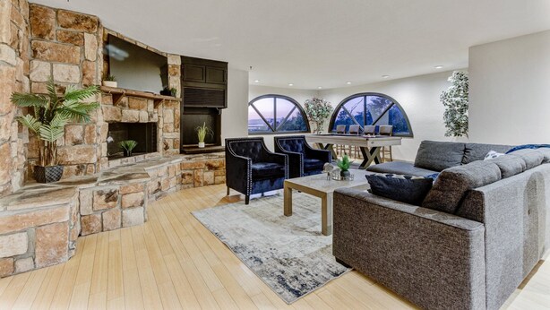 Ein modernes Wohnzimmer mit Kamin aus Stein, gemütlicher Sitzgruppe und großen Fenstern mit Blick ins Freie.