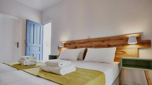 Ein Hotelzimmer mit einem Holzkopfteil, weißer Bettwäsche, einem grünen Nachttisch und einer gelben Tagesdecke.
