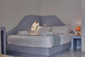 A modern bedroom with a curved headboard, a bed with white linens, a nightstand with a lamp, and a wall-mounted mirror.