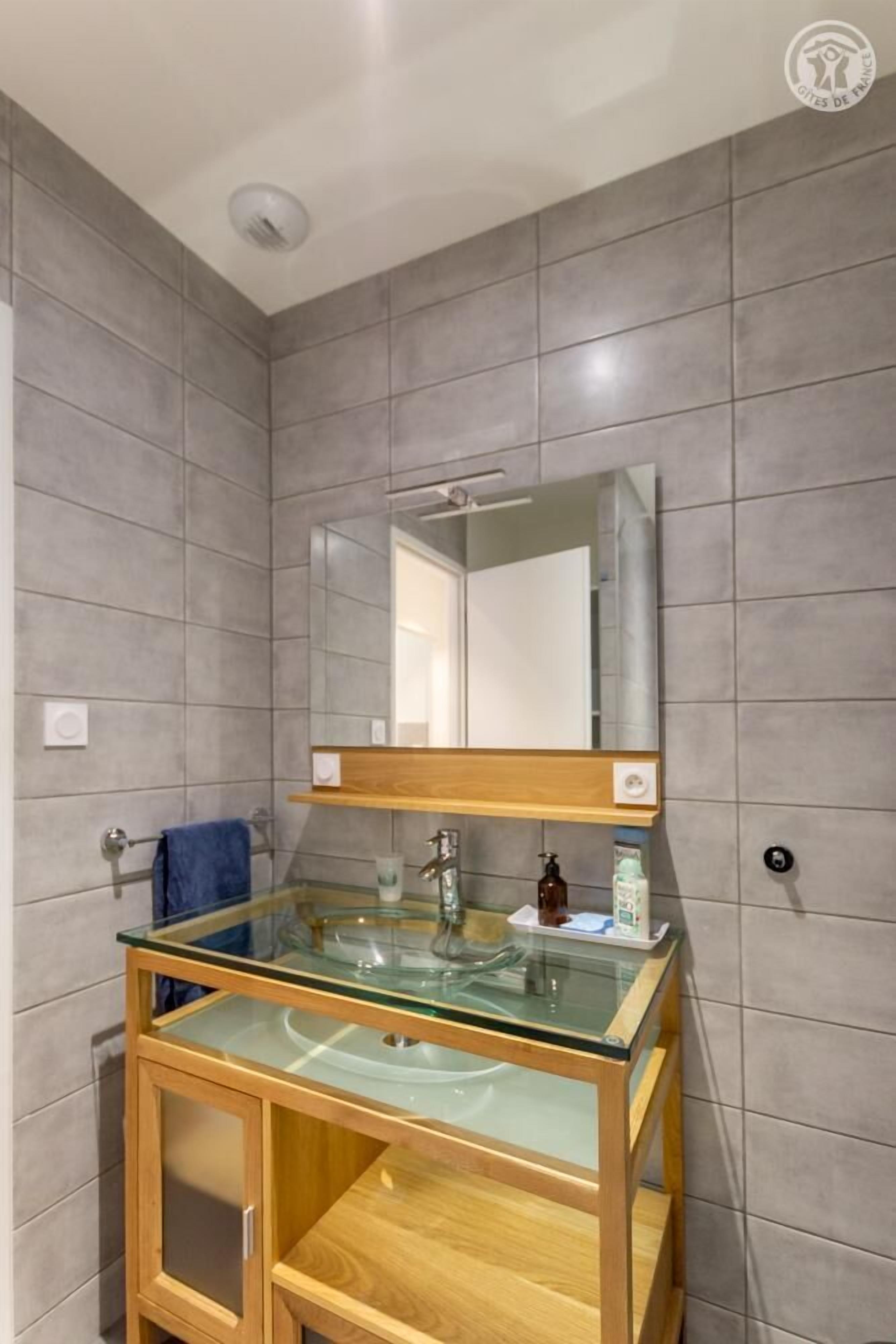 Une salle de bain avec un lavabo en verre, un meuble en bois et un miroir au-dessus.