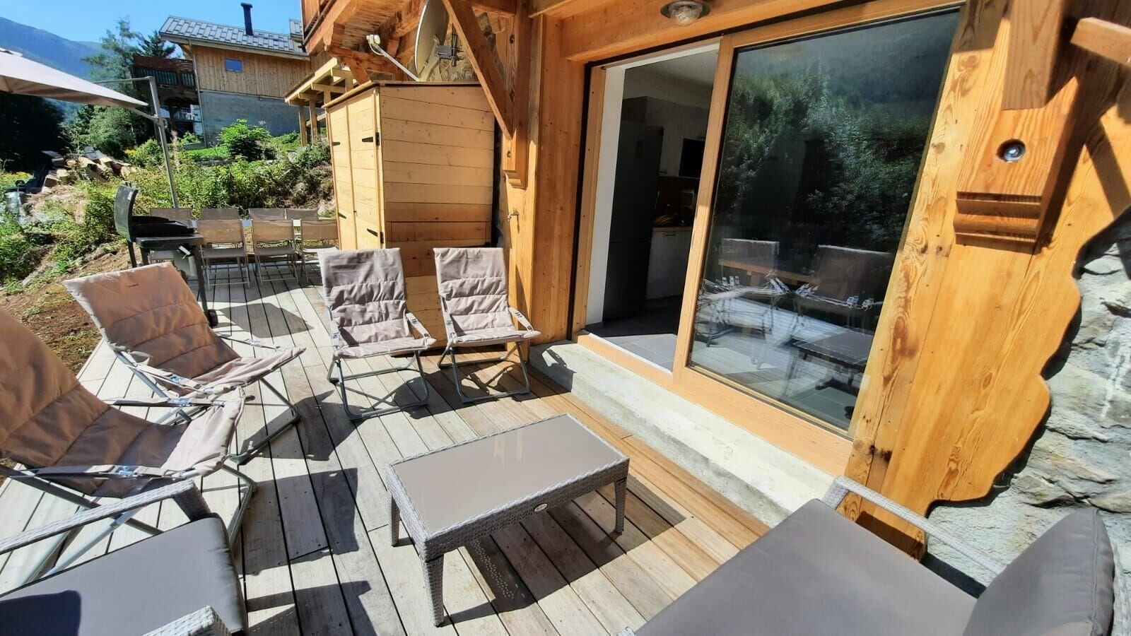 Een houten terras met buitenmeubilair, waaronder stoelen en een tafel.
