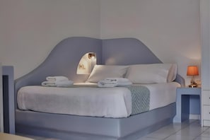 Una camera da letto moderna con una testiera a forma di curva, un letto con lenzuola bianche, un comodino con una lampada e uno specchio fissato alla parete.
