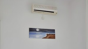 A bedroom with a bed, a wall-mounted air conditioner, and a painting of a night scene.