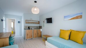 A compact living space with a kitchenette, a dining area, a sofa with yellow cushions, and a TV mounted on the wall.