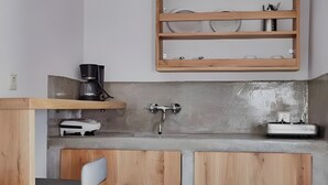 A modern kitchen with wooden cabinets, a concrete countertop, a hanging wicker light fixture, and a built-in shelf above the sink.