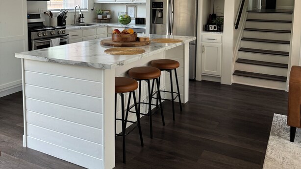Una cocina moderna con armarios blancos, una isla grande con taburetes, un refrigerador de acero inoxidable y un microondas.