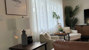 Una sala de estar moderna con un sofá, una mesa de centro, una mesita auxiliar con lámpara y una planta grande.