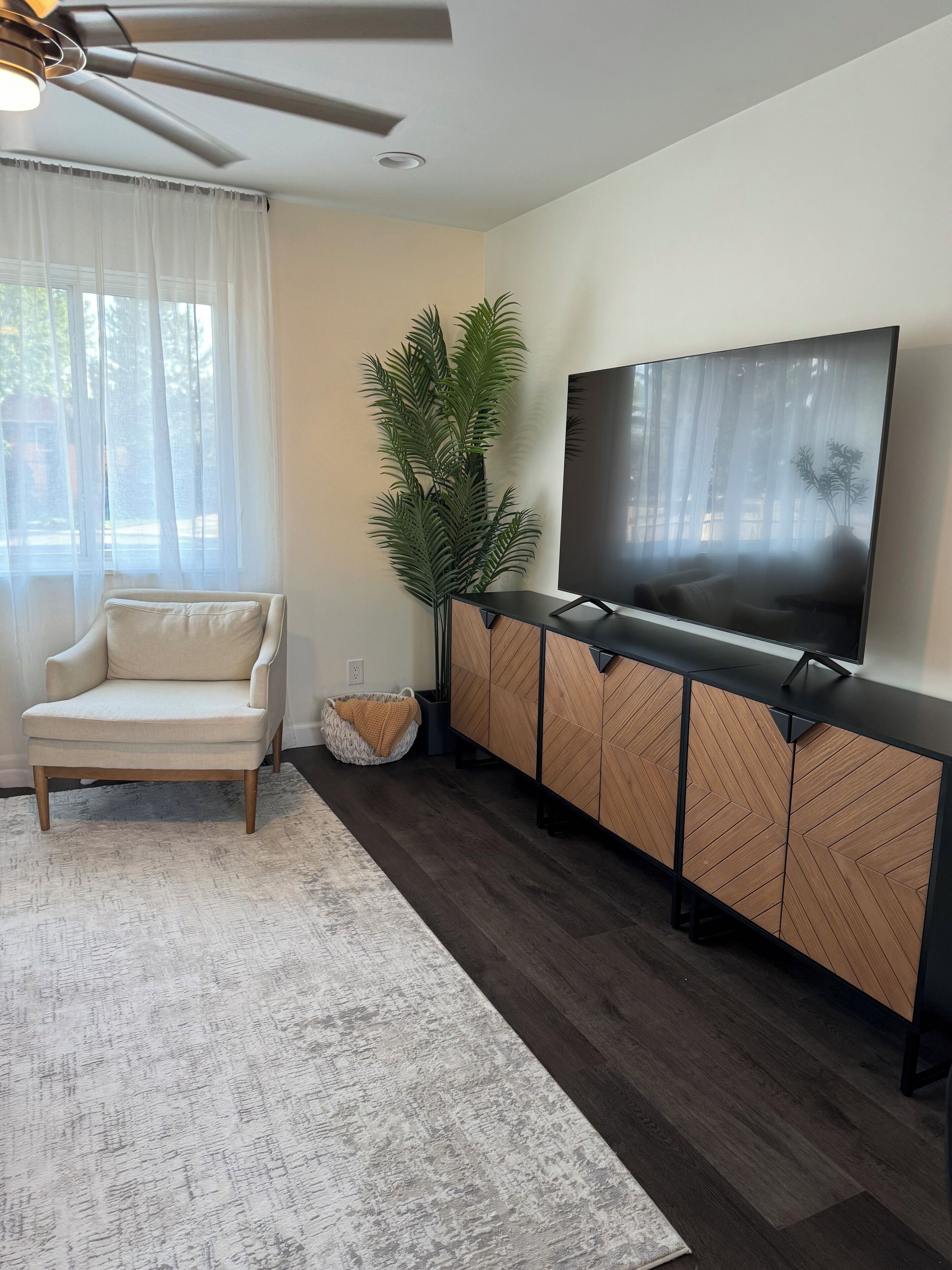 Een woonkamer met een bank, een televisie op een houten kast, een plafondventilator en een grote plant.