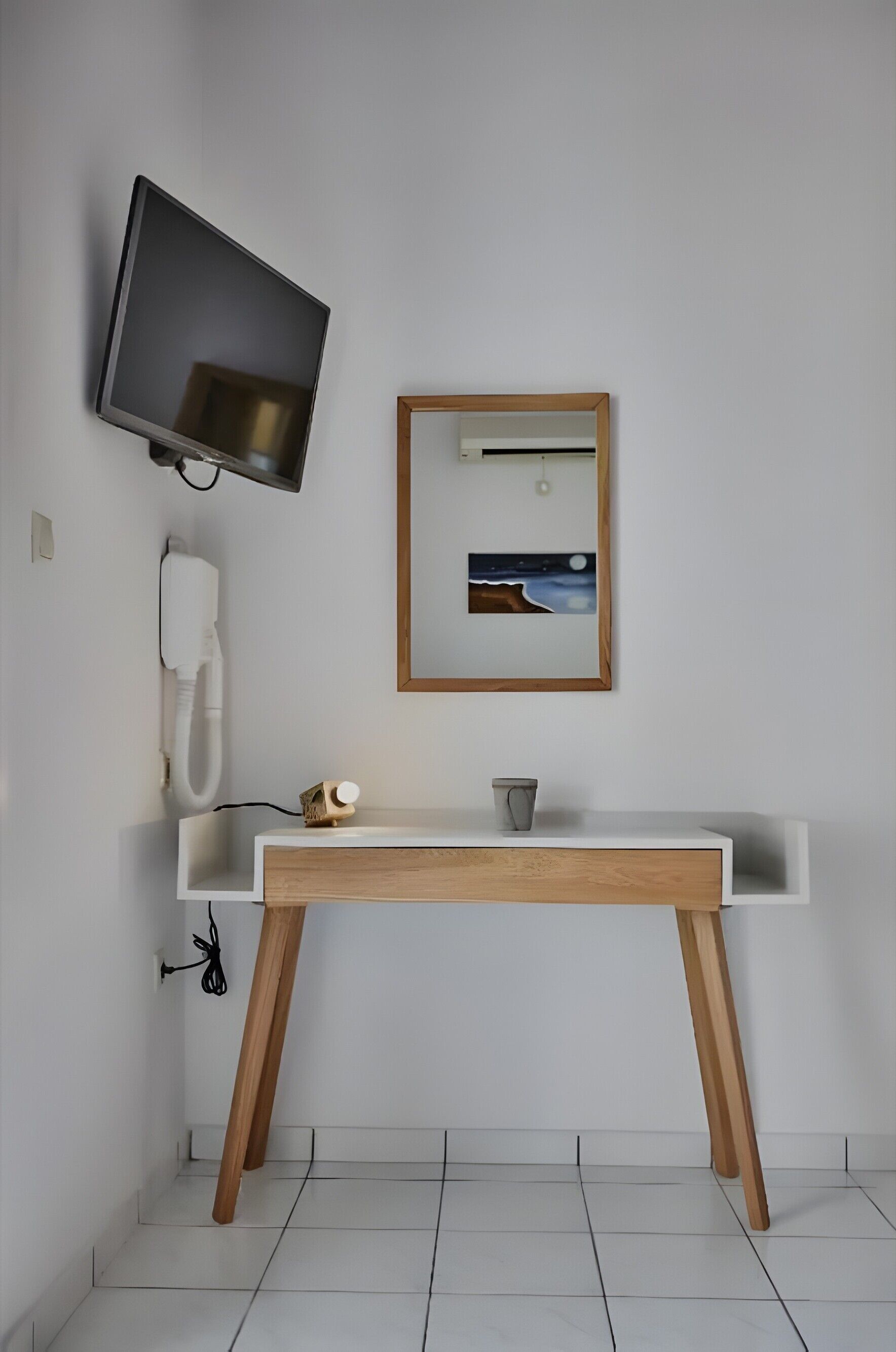 Une salle de bain avec un lavabo blanc, des pieds en bois, un téléviseur fixé au mur, un tableau encadré et un téléphone.
