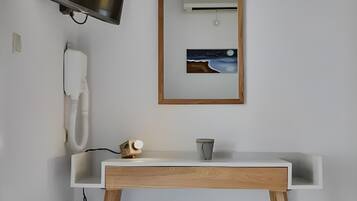 Une salle de bain avec un lavabo blanc, des pieds en bois, un téléviseur fixé au mur, un tableau encadré et un téléphone.