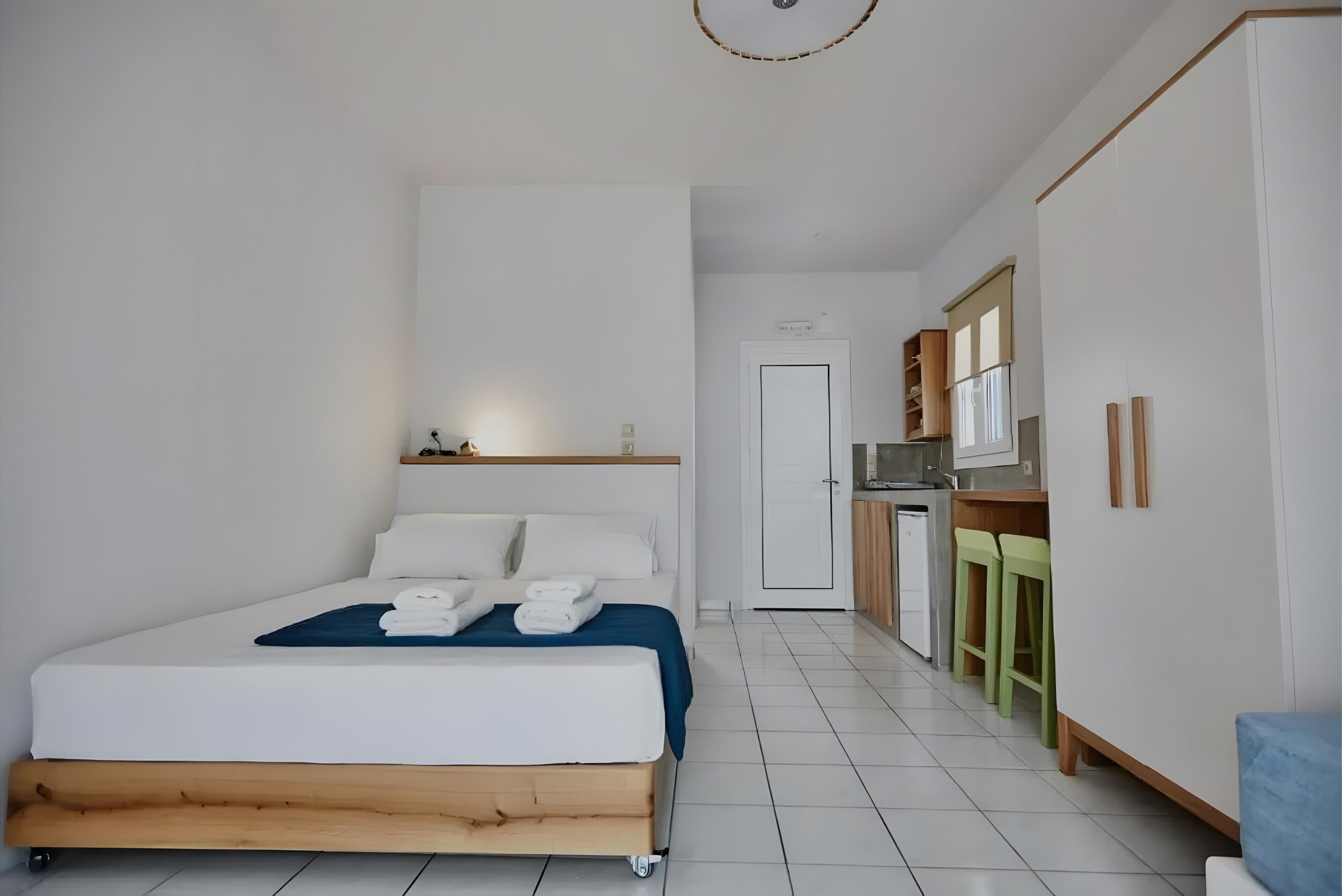 A bedroom with a bed, a small kitchenette, and a door leading to another room.