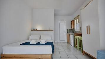 A bedroom with a bed, a small kitchenette, and a door leading to another room.