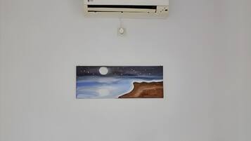 A bed with striped pillows, a wall-mounted air conditioner, and a painting of a night scene.
