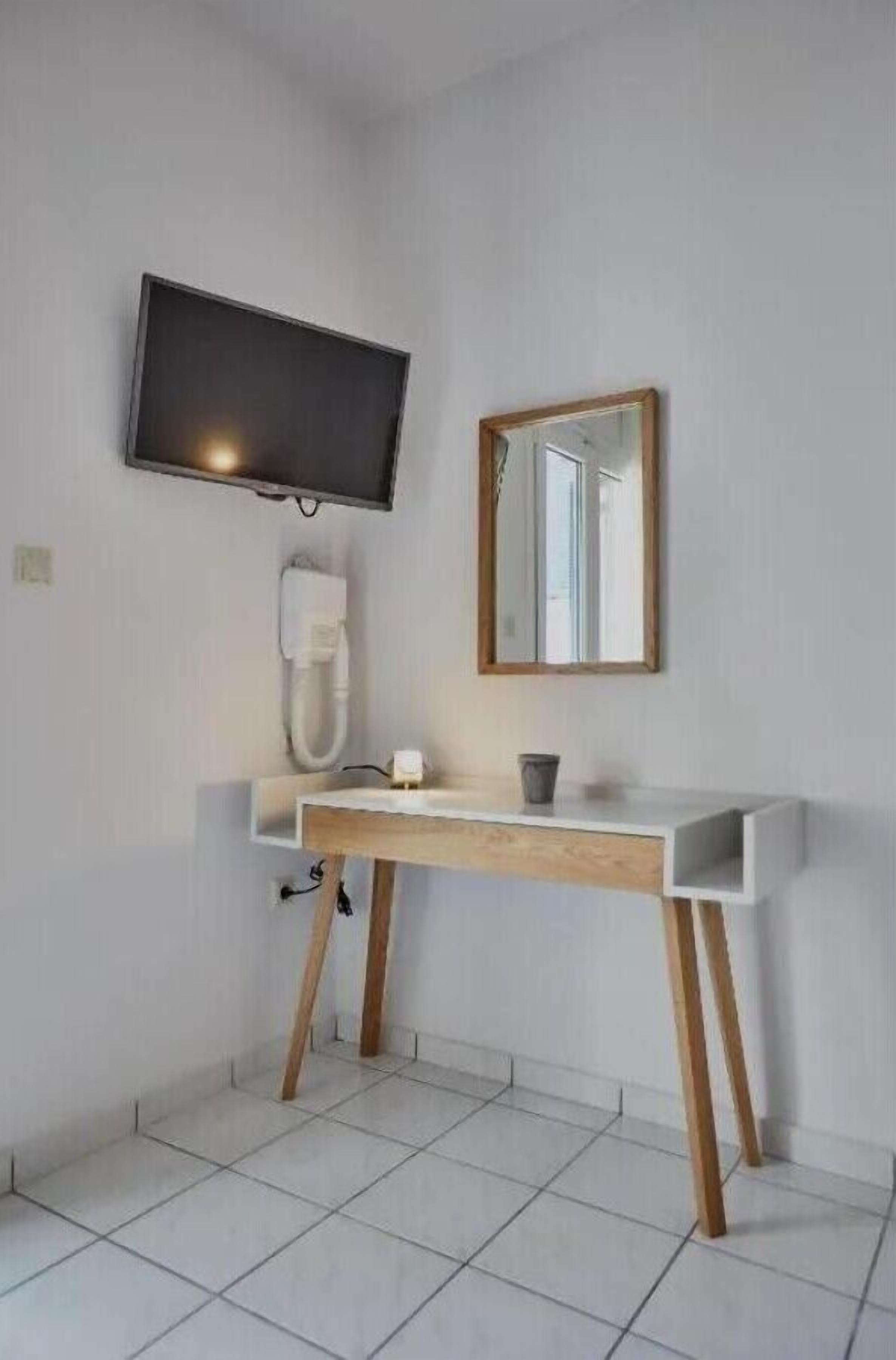 Une salle de bain avec un lavabo blanc, un miroir, un téléviseur fixé au-dessus du lavabo et des toilettes blanches.