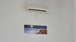 A room with a bed, an air conditioner, and a night scene painting on the wall.