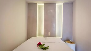 Ein modernes Hotelzimmer mit einem ordentlich bezogenen Bett, einem Nachttisch mit einer Uhr und einer wandmontierten Leuchte.