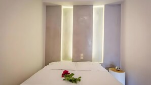 A modern hotel room with a neatly made bed, a bedside table with a lamp, and a wall-mounted light fixture. - Apartment 'Irene 13 Superior  1' with Sea View, Wi-Fi and Air Conditioning (Andros)