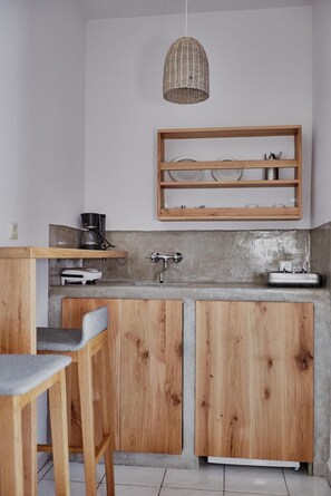 A kitchen with wooden cabinets, a concrete backsplash, a hanging light, and a shelf with dishes.