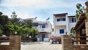 A stone-paved courtyard with white buildings, a stone wall, and a wooden pergola with flowers. - Studio Apartment 'Irene 5 Standard Double 2' with Sea View, Wi-Fi and Air Conditioning (Andros)