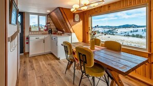 Una cocina acogedora con armarios de madera, una mesa de comedor con sillas y un amplio ventanal con vistas a un paisaje nevado.