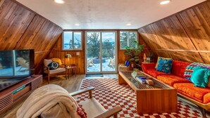 Una habitación acogedora con paneles de madera, un televisor grande, un sofá y una silla.