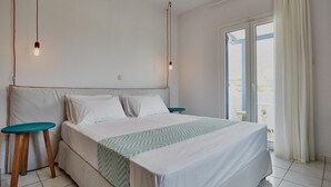 A bedroom with a bed, two bedside tables, a window with curtains, and a view of the outside. - Studio Apartment 'Irene Standard Double 10' with Sea View, Wi-Fi and Air Conditioning (Andros)