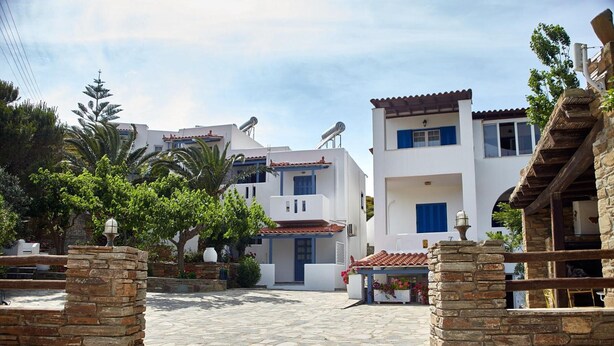 A stone-paved courtyard with white buildings, a stone wall, and a wooden pergola with flowers. - Studio Apartment 'Semi Basement -Superior Apartment' with Mountain View and Air Conditioning (Andros)