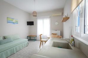 Un espace de vie compact comprenant un canapé, une table à manger, un coin cuisine avec un évier, un téléviseur et une fenêtre avec des rideaux.
