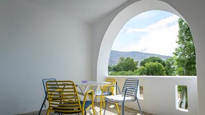 A balcony with a table and chairs, a view of greenery and a mountain, and an arched window. - Studio Apartment 'Semi Basement -Superior Apartment' with Mountain View and Air Conditioning (Andros)