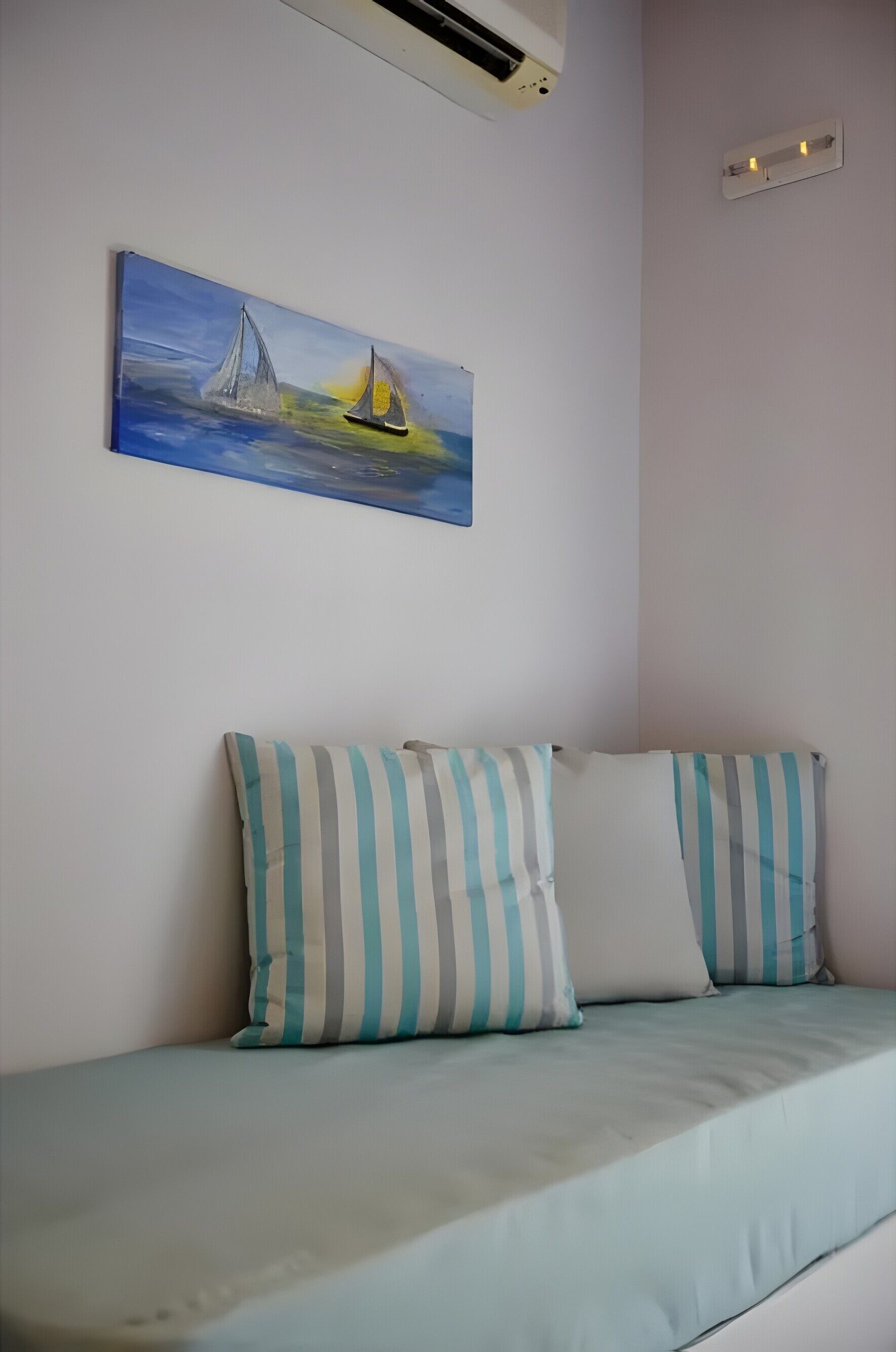 Ein Zimmer mit einem Bett, gestreiften Kissen, einem Segelbootgemälde und einer Klimaanlage.