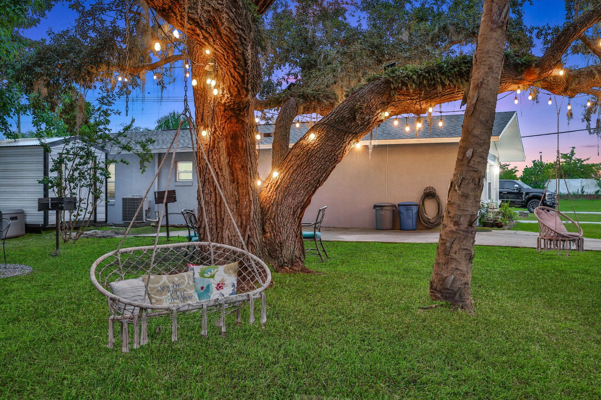A backyard with a swing chair, trees, and string lights.