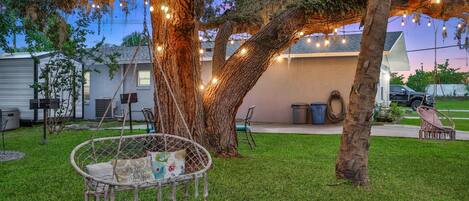 A backyard with a swing chair, trees, and string lights.