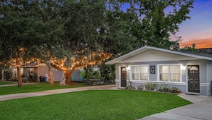 A single-story house with a well-maintained lawn, a porch with outdoor furniture, and a tree with string lights.
