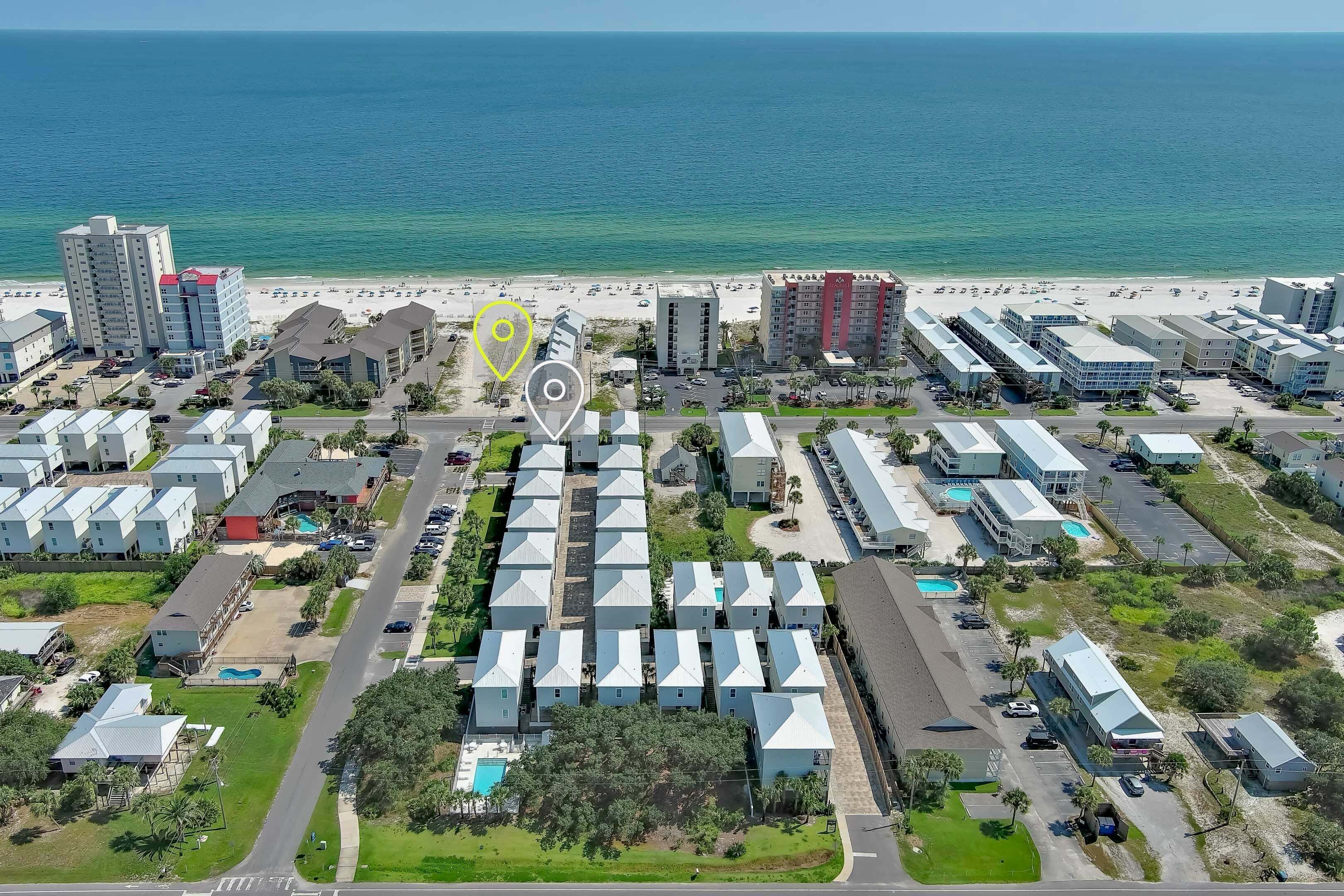 An aerial view of a coastal hotel area with multiple buildings, a beach, and a parking lot.
